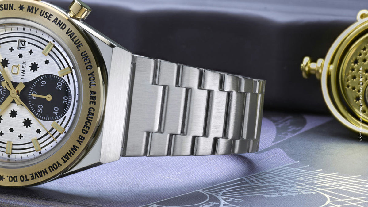 TW2Y75900 Side view of the watch and silver-tone bracelet beside a gold Time-Turner pendant.