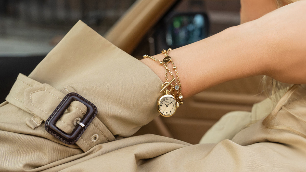 TW6A17700 Gold-tone Cavatina® Mini necklace wrapped around a wrist, with the watch pendant resting beside a beige trench coat cuff.