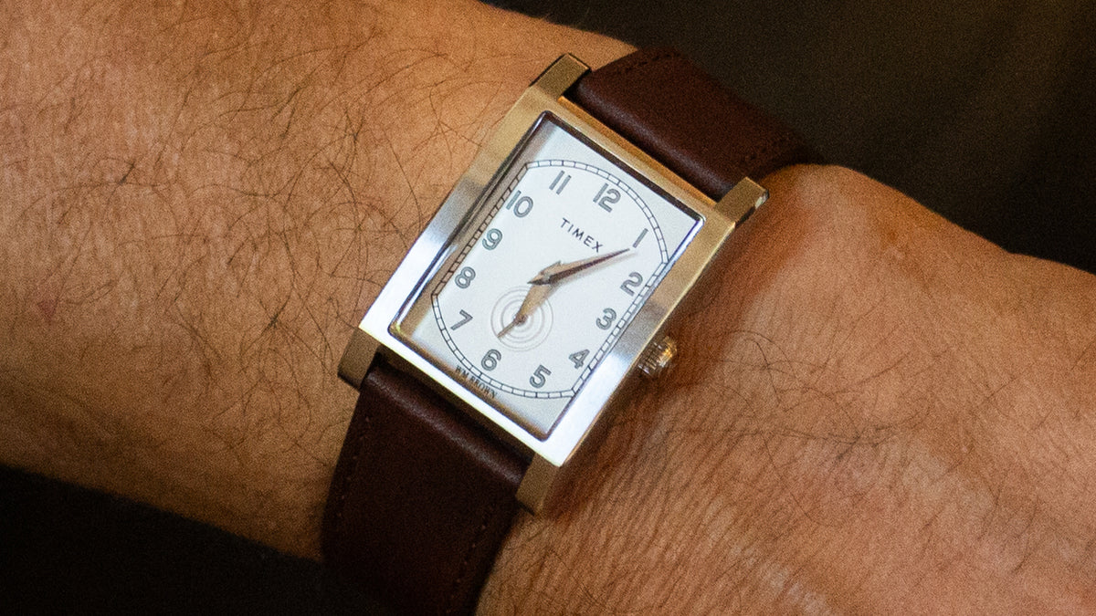 TWG069000 Close-up of a WM Brown x Timex watch on a wrist, showing its white dial, Arabic numerals, small seconds subdial, and brown leather strap.