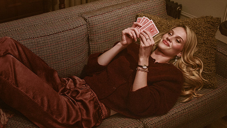 Gifts for Her - Woman reclining on a patterned sofa, holding playing cards and wearing a gold-tone Timex watch.