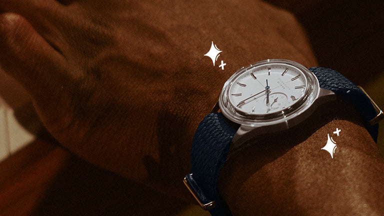Luxe Gifts - Close-up of a Timex watch with a white dial, silver-tone case and navy strap worn on a wrist.