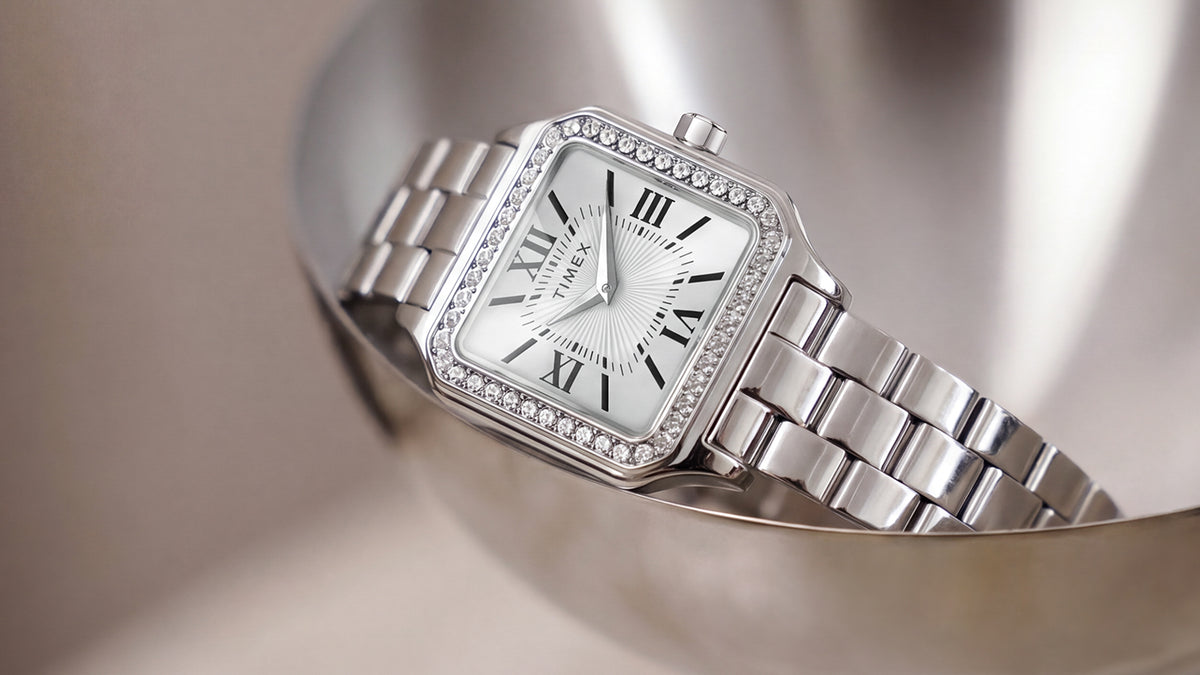 TW2Y90300 Close-up of the Timex Addison watch’s white Roman numeral dial, crystal-lined bezel, and polished silver-tone bracelet in a metal dish.