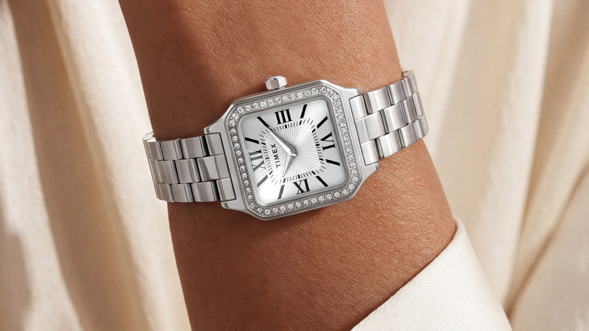 Close-up of the Timex Addison watch on a wrist, highlighting its crystal-lined rectangular bezel, white dial, and silver-tone link bracelet.