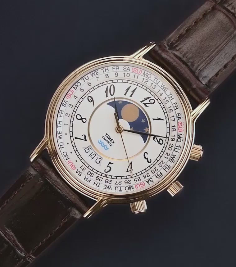 Timex 1990 Moon Phase and Calendar Dial Reissue watch with a gold-tone case, detailed white dial, and brown leather strap rotating against a dark background.