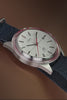 Marlin Jet America 250 automatic watch with a white dial, red bezel accent, red seconds hand, and blue woven strap displayed on a reflective blue surface.