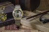 TW2Y75900 Harry Potter x Q Timex Time Turner Chronograph with a gold-tone bezel, star-patterned dial and silver-tone bracelet, displayed beside a Time-Turner necklace, wand, glasses and books.
