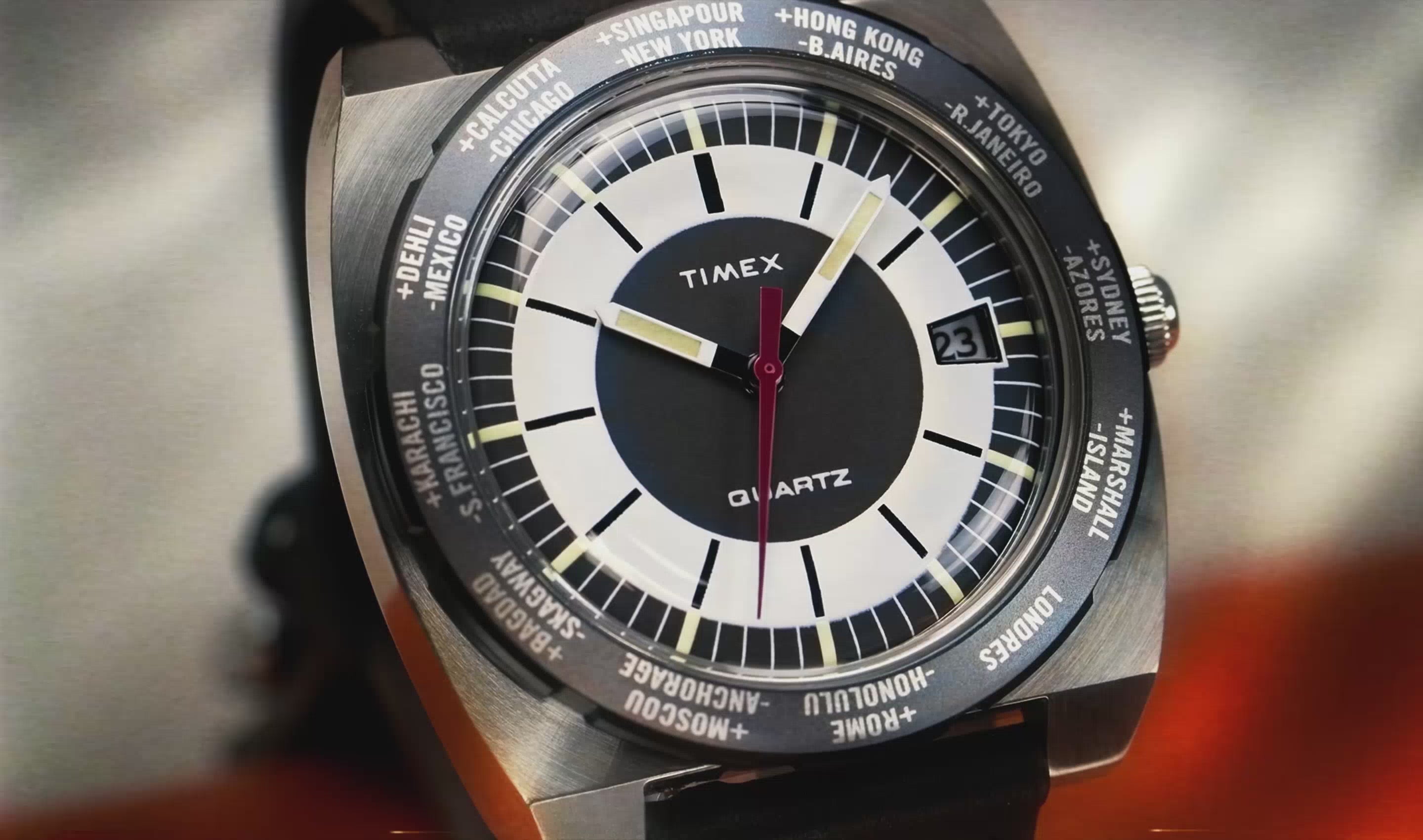 A rotating product video of the Q Timex® 1972 World Time watch, featuring its retro-inspired cushion-shaped case, multi-city bezel, and bold tri-color dial with red seconds hand. The watch slowly turns to showcase its domed crystal, side crown, brown stitched leather strap, and polished stainless-steel case back, set against a clean studio backdrop.