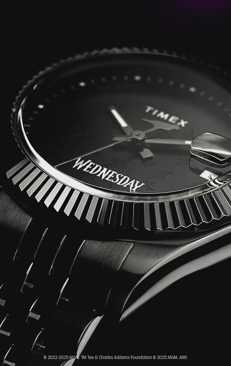 Video for the Timex x Wednesday Timex Legacy watch, featuring gothic-inspired visuals and atmospheric lighting. The video highlights the watch’s sleek black stainless-steel bracelet, textured black dial with raven silhouettes, and a red skull icon in the date window. Close-up shots emphasize the refined fluted bezel, glow-in-the-dark hands, and the engraved caseback.
