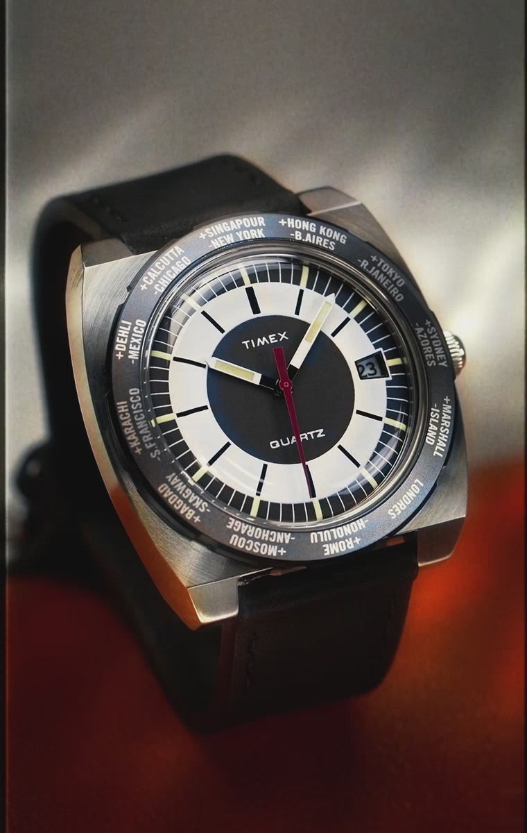 A rotating close-up video of the Q Timex® 1972 World Time wristwatch, showcasing its retro-futuristic design with a cushion-shaped stainless-steel case, world time bezel, and bold dial detailing. The video highlights the watch's vintage styling, domed acrylic crystal, and dual time zone functionality as it spins against a clean, minimal backdrop.