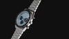 Q Timex Chronograph watch rotating against a black background, showcasing its light blue dial, black chronograph subdials, tachymeter bezel, and stainless-steel bracelet.